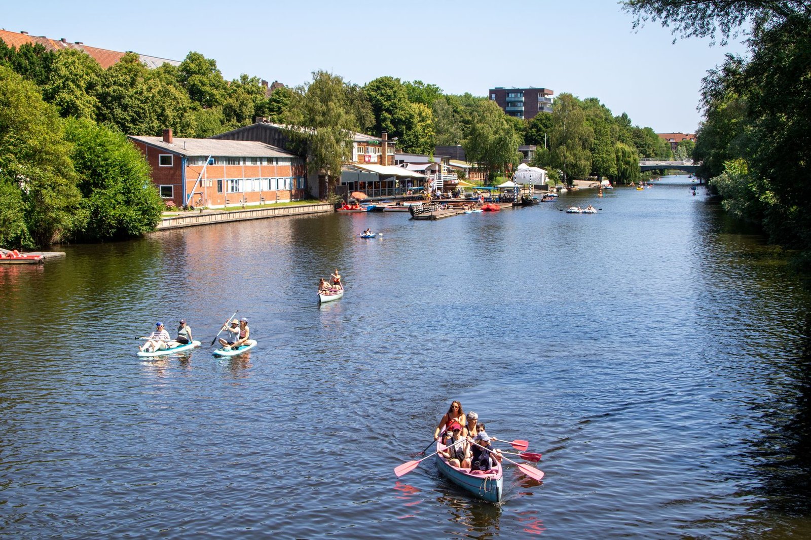 A picturesque summer scene in Hamburg with people canoeing on a canal under a blue sky.